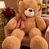 Large teddy bear with a plaid bow sitting beside a bouquet of red roses