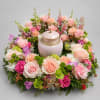 A pale pink ceramic urn framed by a ring of blush roses
