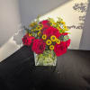 Red roses and yellow button flowers in a square glass vase