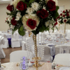 Tall centerpiece with red roses and white flowers in a gold stand