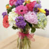 Mixed bouquet of pink, purple, yellow, and white flowers in a glass vase