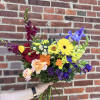 Colorful hand-tied bouquet with yellow gerbera daisies, red roses, purple irises, and assorted mixed flowers