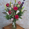 A garden-style mix of roses and lilies arranged upright in a clear