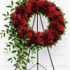 Deep crimson roses and deep burgundy carnations form a large, circular sympathy