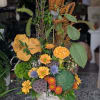 Tall autumn floral arrangement with orange blooms and textured seed heads in a birch vase