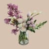 Lavender dendrobium orchids arch above white mini calla lilies and soft blush-to-cream