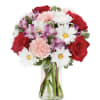 Daisy, carnation, red roses in a clear glass vase.