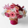 Compact arrangement of pink roses, gerbera daisies, lilies and white orchids in a pink cylinder vase.
