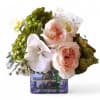 Low arrangement of peach roses and white orchid in a square purple glass vase with a card