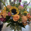 Mixed bouquet with a sunflower, peach roses, and purple blooms in a glass vase