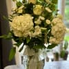 White floral arrangement in a clear glass vase with a ribbon bow