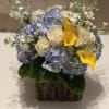 Blue hydrangeas with white roses and yellow calla lilies in a bark-covered container