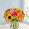Colorful bouquet of sunflowers, roses, lilies, and mixed blooms in a glass vase