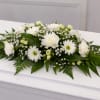 A low, elongated white casket spray arranged to convey quiet reverence-the kind