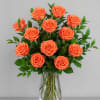 A dozen vibrant orange roses arranged in a clear glass vase creates