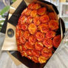 Large bouquet of tightly packed orange and yellow roses wrapped in tan and black paper