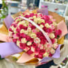 Large round bouquet of hot pink, light pink, and cream roses wrapped in multicolored paper.