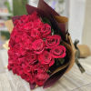 Large bouquet of red roses wrapped in brown and burgundy paper on a table