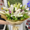 Hand-tied bouquet of white lilies, calla lilies, and roses with small purple blooms wrapped in brown paper
