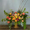 Large mixed flower arrangement in a gold vase with peach and pink blooms
