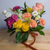 Bouquet of yellow roses, pink carnations, and white lisianthus in a wrapped vase