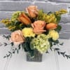 Peach roses and bright orange lilies meet clustered green hydrangea blooms in