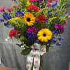 Mixed bouquet in a glass vase with yellow daisies, carnations, and blue flowers