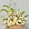 White floral arrangement in a woven basket with tall green accents
