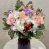 Pink and white mixed bouquet with purple accents and red berries in a faceted dark purple glass vase