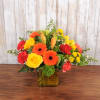 Bright mix of orange, yellow, and red flowers in a yellow glass cube vase
