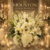 This elegant composition features lush white hydrangeas, creamy ivory roses, graceful white