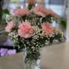 Pink carnation and white filler flower bouquet arranged in a clear glass jar