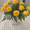 Yellow roses arranged in a white vase with fern foliage