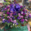 A dramatic, elegant casket spray in shades of purple, pink, white and