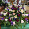 A graceful, low-profile casket spray in pink, purple, white, and green creates