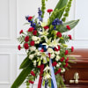 Standing funeral spray with white lilies, red carnations, and blue flowers