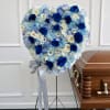 Heart-shaped blue and white floral funeral spray beside a casket