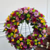 Large floral wreath with roses and daisies on a stand beside a casket