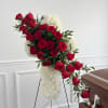Red roses and white flowers arranged on a standing easel beside a casket