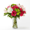 Bright pink roses and carnations with green button mums and white blooms in a clear glass vase.