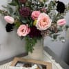 Mixed pink and burgundy bouquet in a tall vase with a box of macarons in front
