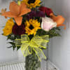 Mixed bouquet with sunflowers, lilies, roses, and a yellow bow in a glass vase