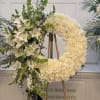 A graceful standing wreath of cream-white roses, hydrangeas and white lilies arranged