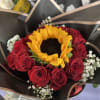 Hand-tied bouquet with a large yellow sunflower, red roses, and white filler flowers in black wrapping paper