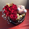 Heart-shaped box with red roses, a teddy bear, and chocolates
