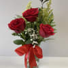 Three red roses in a clear glass vase with a red ribbon