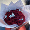 Hand-tied bouquet of red roses with white filler flowers wrapped in soft pink paper