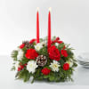 Red candles in a holiday floral centerpiece with white flowers and pinecones