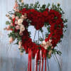 Heart-shaped red rose wreath on a stand with pink accents and ribbon tails