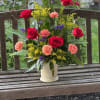 Mixed bouquet of red roses, peach carnations, and purple filler in a white vase